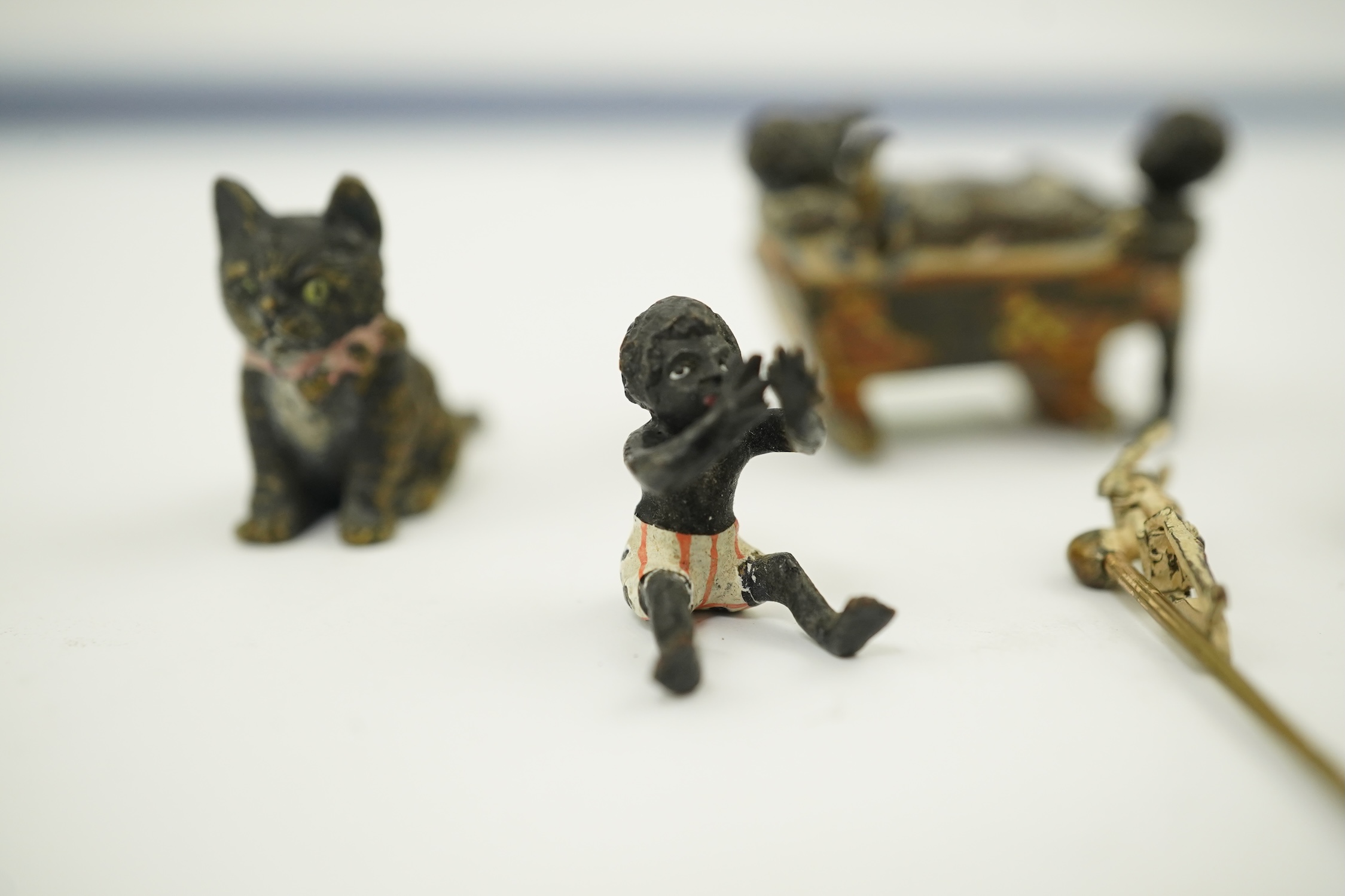 Four novelty miniature cold painted bronzes; black boy with cradle, black baby, cat and pig and a similar articulated arm skeleton stickpin,7cm long. Condition - some chipping to paint